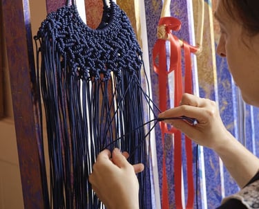 Bolsa de macramé azul marino hecha a mano siendo tejida por una artesana en un telar vertical.
