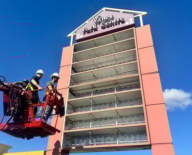 Technicians in a bucket lift repairing the Valley Park Centre pylon sign under a clear blue sky.