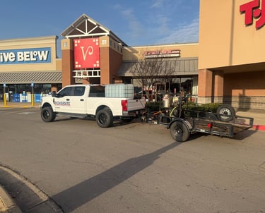 White service truck with trailer parked outside retail stores for commercial property maintenance.