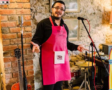 a man dressed in 1950s costume for a themed murder mystery. He is smiling and wearing a pink apron.