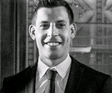 A black and white professional portrait of a smiling man in a suit and tie.