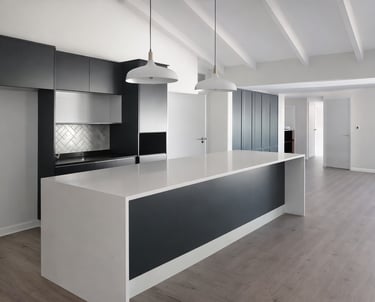 Modern minimalist kitchen with white quartz island, black cabinetry, and vaulted beamed ceilings.