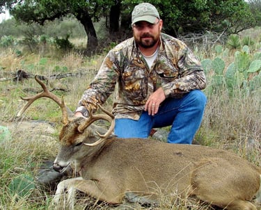 A hunter posing with a trophy whitetail buck in the rugged Texas Hill Country terrain near prickly pear cactus.