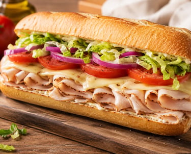 A gourmet turkey sub sandwich with melted cheese, fresh lettuce, tomatoes, and red onions on a toasted baguette.