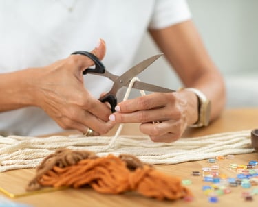 Manos sobre una mesa cortando un hilo para realizar un bordado en macramé