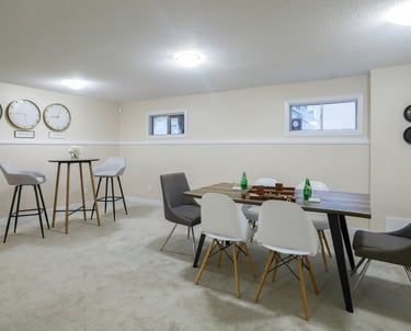 Modern finished basement featuring a wooden dining table with Eames-style chairs and a high-top bistro set.
