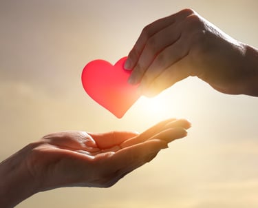 Hand placing a red heart into another person’s open hands