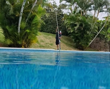 Técnico profissional de piscinas usando uma vara telescópica para limpar uma piscina de quintal cerc