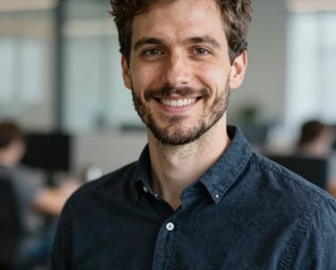 Professional portrait of a male lead developer with a friendly smile, set against a blurred modern office background. International / European setting, soft light.
