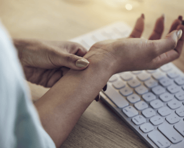 A person holding their painful wrist over a keyboard, illustrating carpal tunnel syndrome and RSI symptoms.