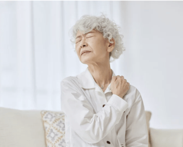 Senior woman experiencing shoulder pain and muscle tension while sitting on a sofa.