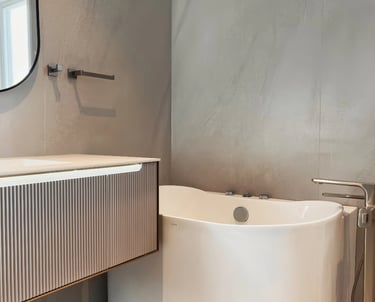 Modern bathroom interior featuring a white freestanding bathtub and fluted vanity cabinet against gray textured walls.