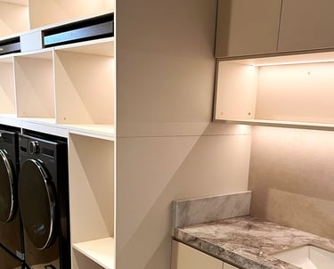 Modern laundry room with black front-load appliances, marble countertops, and built-in white storage cabinets.