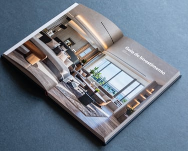 A high-end photography book or brochure lying on a slate blue surface, titled 'Guia de Investimento', showing interior design details of a luxury Brazilian penthouse.