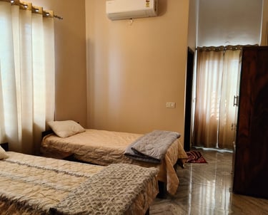 Cozy bedroom with twin beds, neutral curtains, and wall-mounted air conditioning unit for comfort.