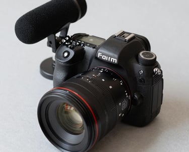 A professional photograph of an expensive DSLR camera and a studio microphone on a clean, light gray surface. The composition is minimalist and high-end.