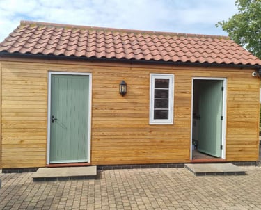 Exterior of a small building, with walls covered in wood-panelling and doors painted green..