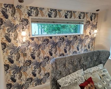 Cosy living room, with a white, fern-style feature wall, grey sofa, and thin upper window.