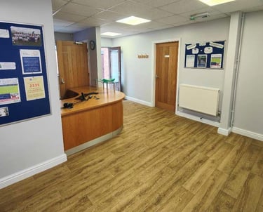 Modern reception area, with painted off-white walls, wood flooring/desk, and a drop-ceiling.