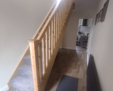 Modern entrance hallway, with painted white walls/ceiling, light-wooden banister, and wood flooring.