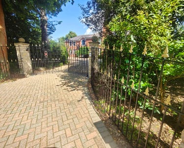 Exterior brick driveway, with painted black fencing and gate, adorned with gold arrowheads.