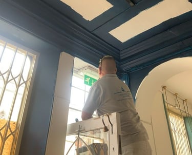 An in-progress navy-blue room, with a painter using a ladder to finish a doorway.