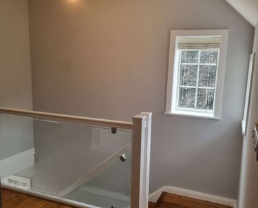 Top of a staircase, with glass banisters, wooden flooring, grey walls, and white detailing.