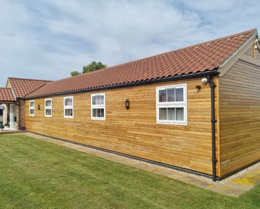 Exterior of long bungalow, with wood panelling on all walls, white windows, and maroon roof tiles.