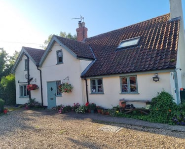Exterior of large, painted-cream cottage, with light green door/window frames, and gravel drive.
