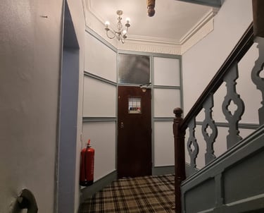 Bottom of a stairway leading to a door, with grey walls and green/dark-grey detailing and banister.