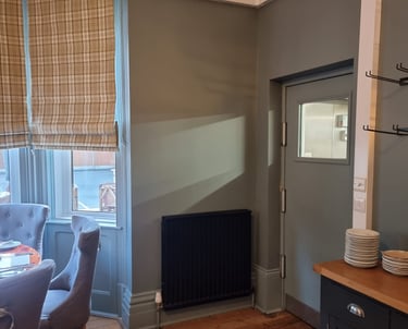 Corner of restaurant dining room, with dark-grey door, a window, and black radiator.