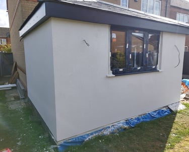 Exterior of a small extension being built on a residential home, with walls painted white.