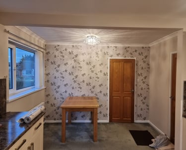 A square dining room, with cream walls, a white ceiling, and a feature wall with a vine-like motif.