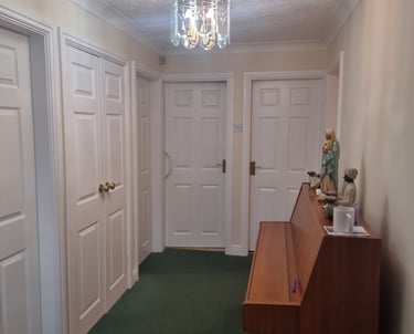 A freshly painted white hallway, with four white doors, green carpet, and a wooden organ.