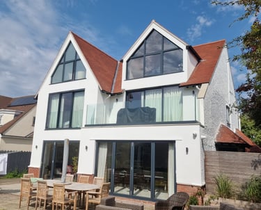 Exterior front of a 3-storey home, that has white-painted walls and many large windows/glass doors.
