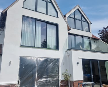 Exterior front of a 3-storey home, that has white-painted walls and many large windows/glass doors.