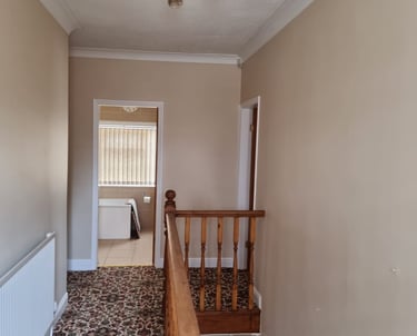 A small upstairs hallway, with painted cream walls, white doorframes, and brown patterned carpet.