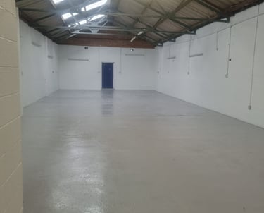 A painted white industrial unit, with a blue door and corrugated roof.