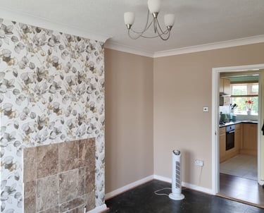 An unfurnished living room, with pink/cream walls, except a wall with white, floral wallpaper.