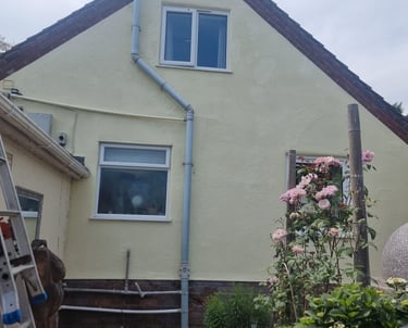 Exterior of a large house, with cream-painted walls, white window frames, and unpainted brick base.