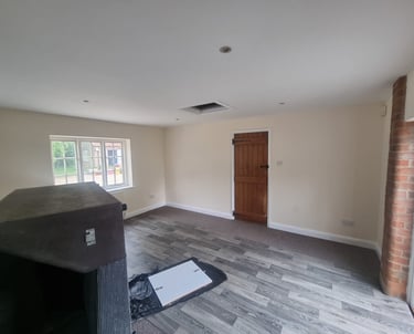 A large unfurnished room, with walls and ceiling painted white, and a rustic brown wooden door.