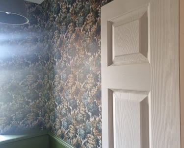 A room with forest-like wallpaper, green-painted wooden panels underneath, and a cream door.