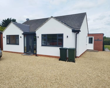 Exterior of a painted-white bungalow, with a black-tiled roof and black detailing.