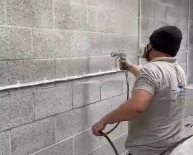 LPAD staff using a paint sprayer on an industrial cinderblock wall.