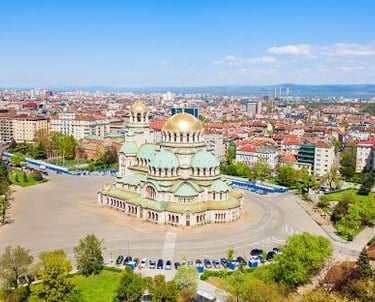 A sunny view of Vitosha Boulevard in Sofia, Bulgaria, featuring a tree-lined pedestrian street and mountain views.