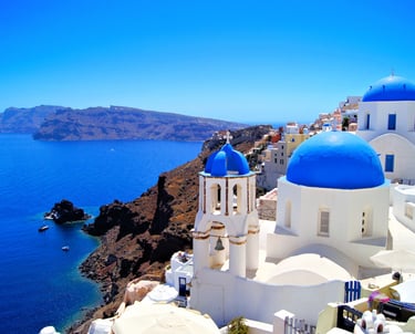 Iconic blue domed churches in Oia Santorini overlooking the Aegean Sea and caldera cliffs.