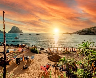 Golden sunset over Cala d'Hort beach in Ibiza with views of Es Vedra island and boats.