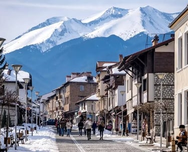 Tourists walking through the snowy streets of Bansko ski resort town with Pirin Mountains in the background.