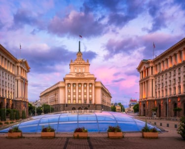 The Largo square in Sofia, Bulgaria featuring the National Assembly building under a sunset sky.
