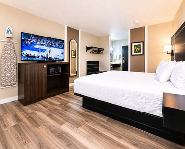Modern hotel room featuring a king-sized bed, hardwood floors, and a flat-screen TV playing basketball